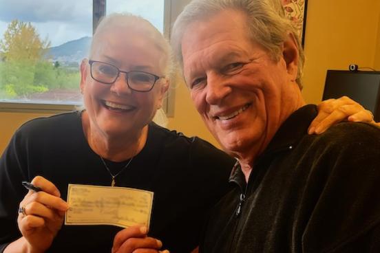 Two people smiling while holding a check