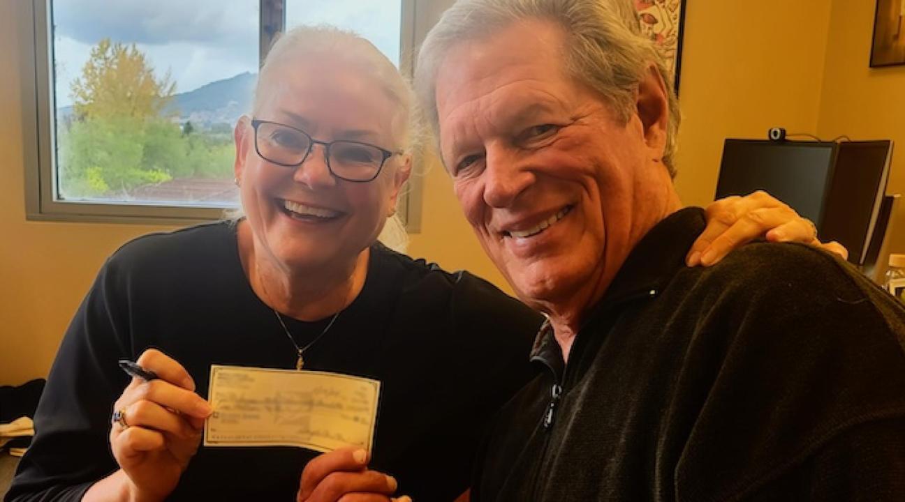 Two people smiling while holding a check