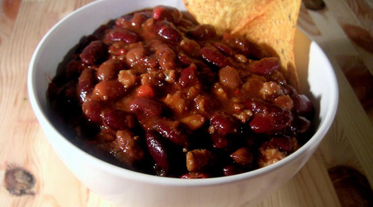 a bowl of chili with two tortilla chips to the side.