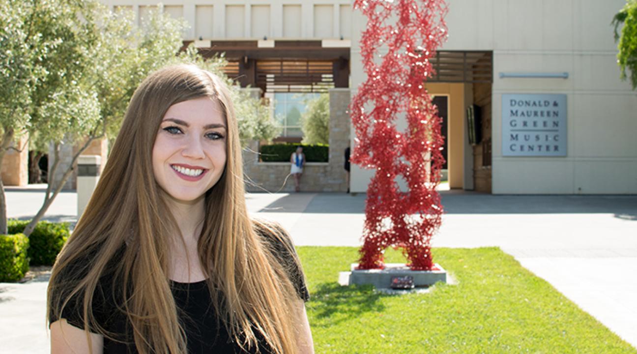 Kellie Gillespie next to her sculpture, connected, in front of the green music center