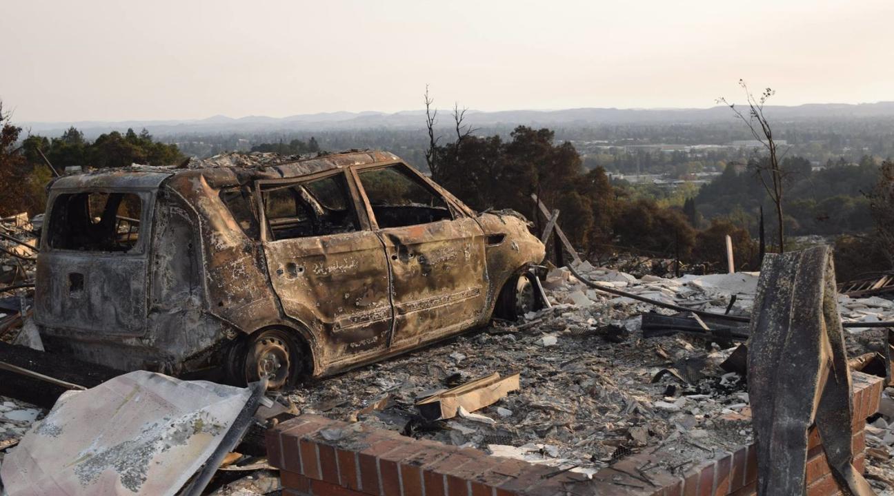 A destroyed car looks out over Santa Rosa to the west on Alturia Drive near the boulders at Fountaingrove, where hundreds of homes were lost in the Oct. 9 firestorm. // Photo by Paul Gullixson