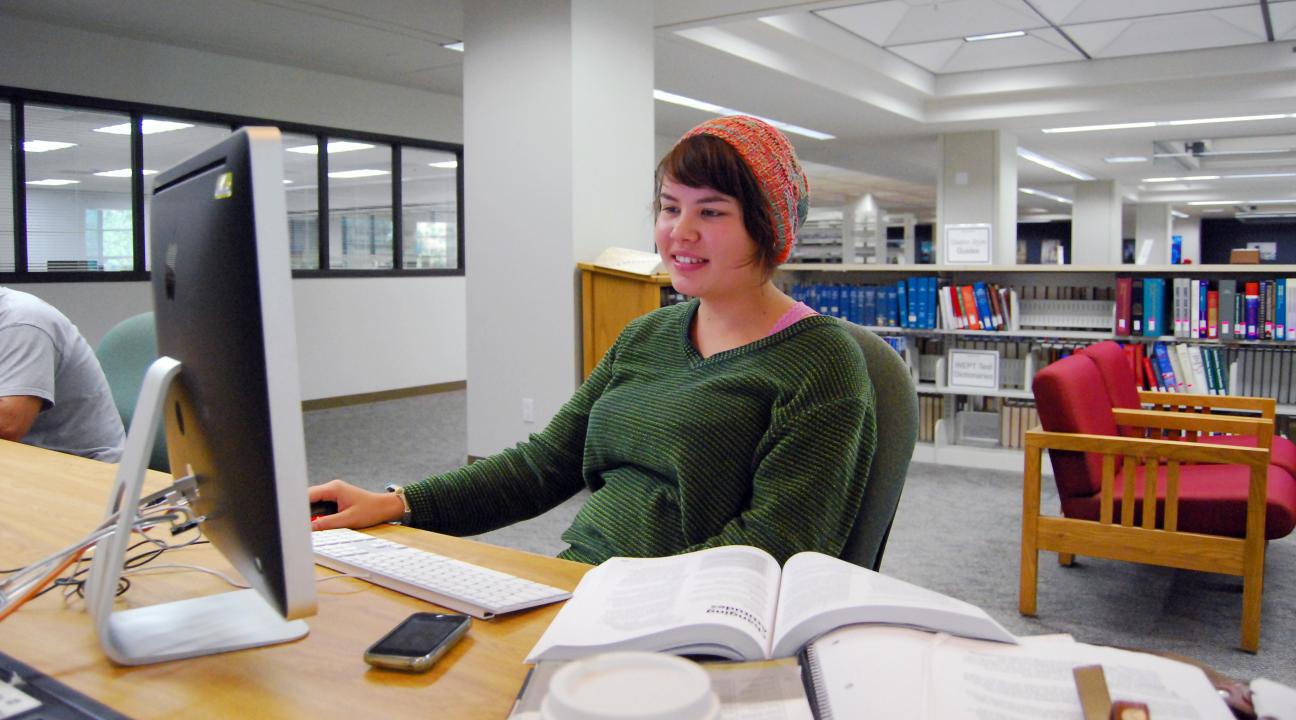 Student using computer and books in library