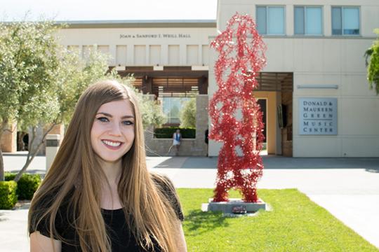 Kellie Gillespie next to her sculpture, connected, in front of the green music center