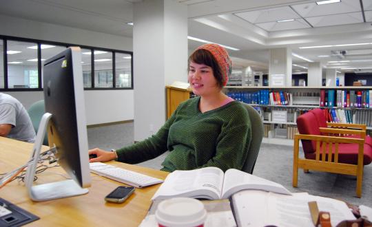 Student using computer and books in library