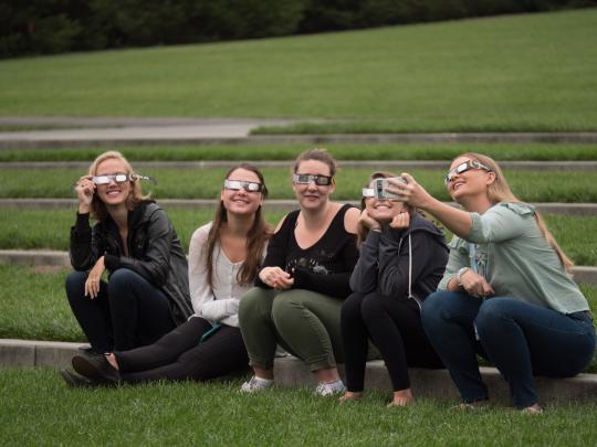 Students wear eclipse glasses at Convocation 2017 outside Weill Hall